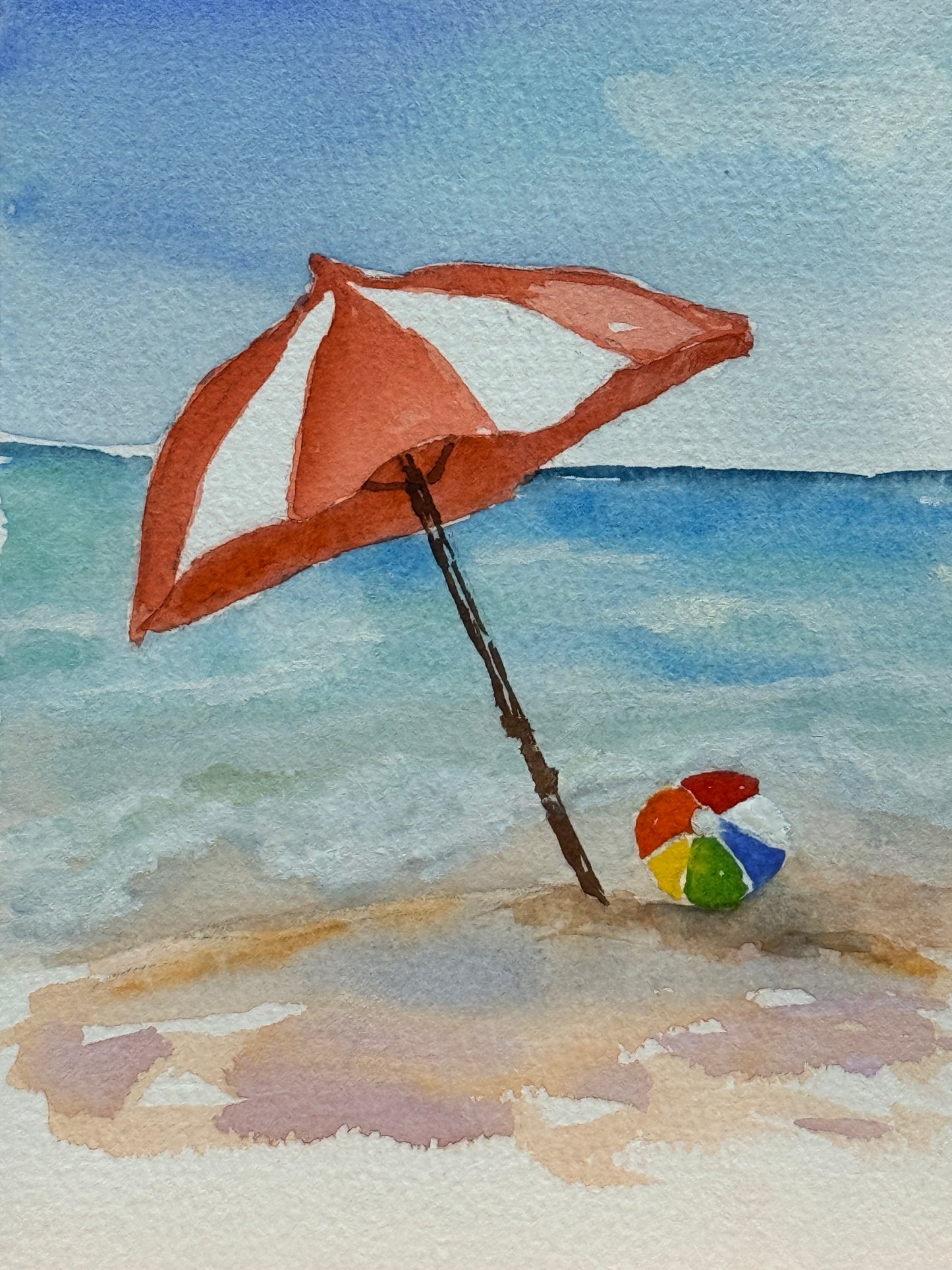 Watercolor painting of a beach scene with an open red umbrella and colorful ball on sand.