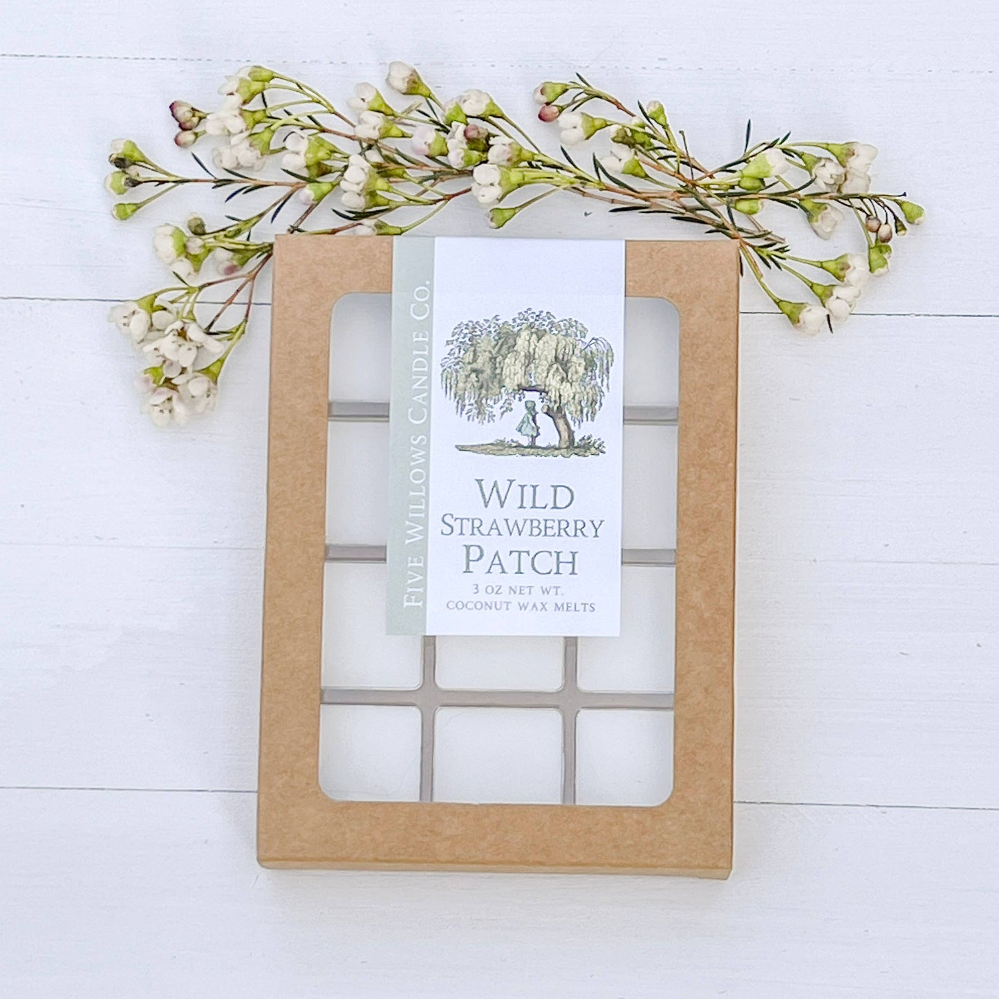 Wax melt packaging labeled 'Wild Strawberry Patch' with decorative floral elements on a white wooden background.