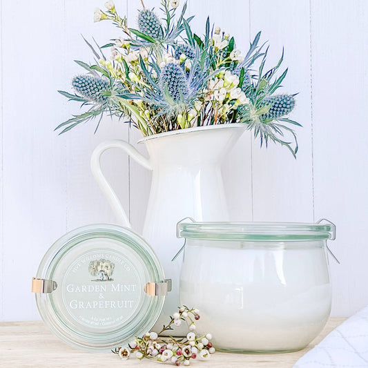 Decorative pitcher with flowers and two glass containers on a wooden surface.