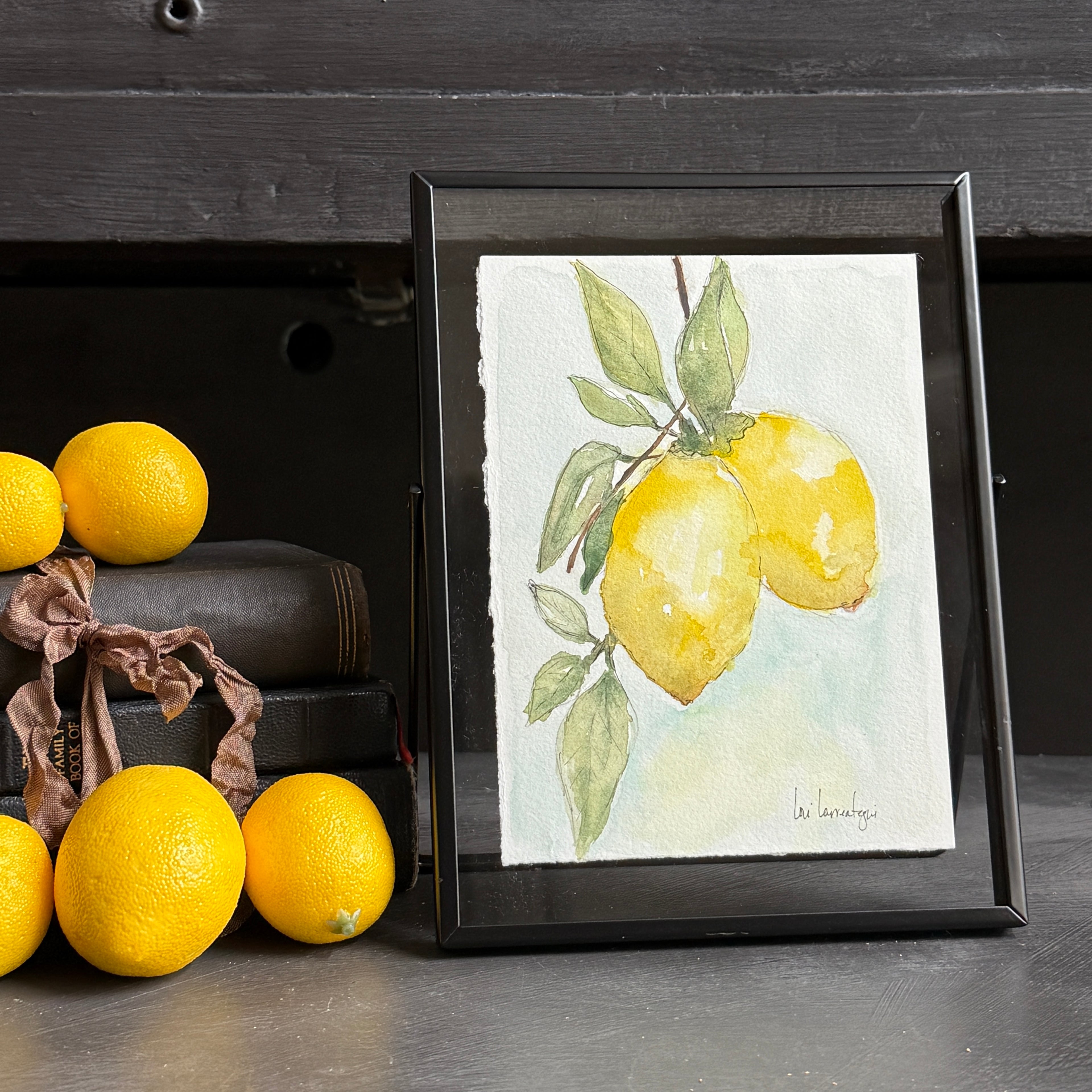 Framed artwork of lemons on a table with real lemons