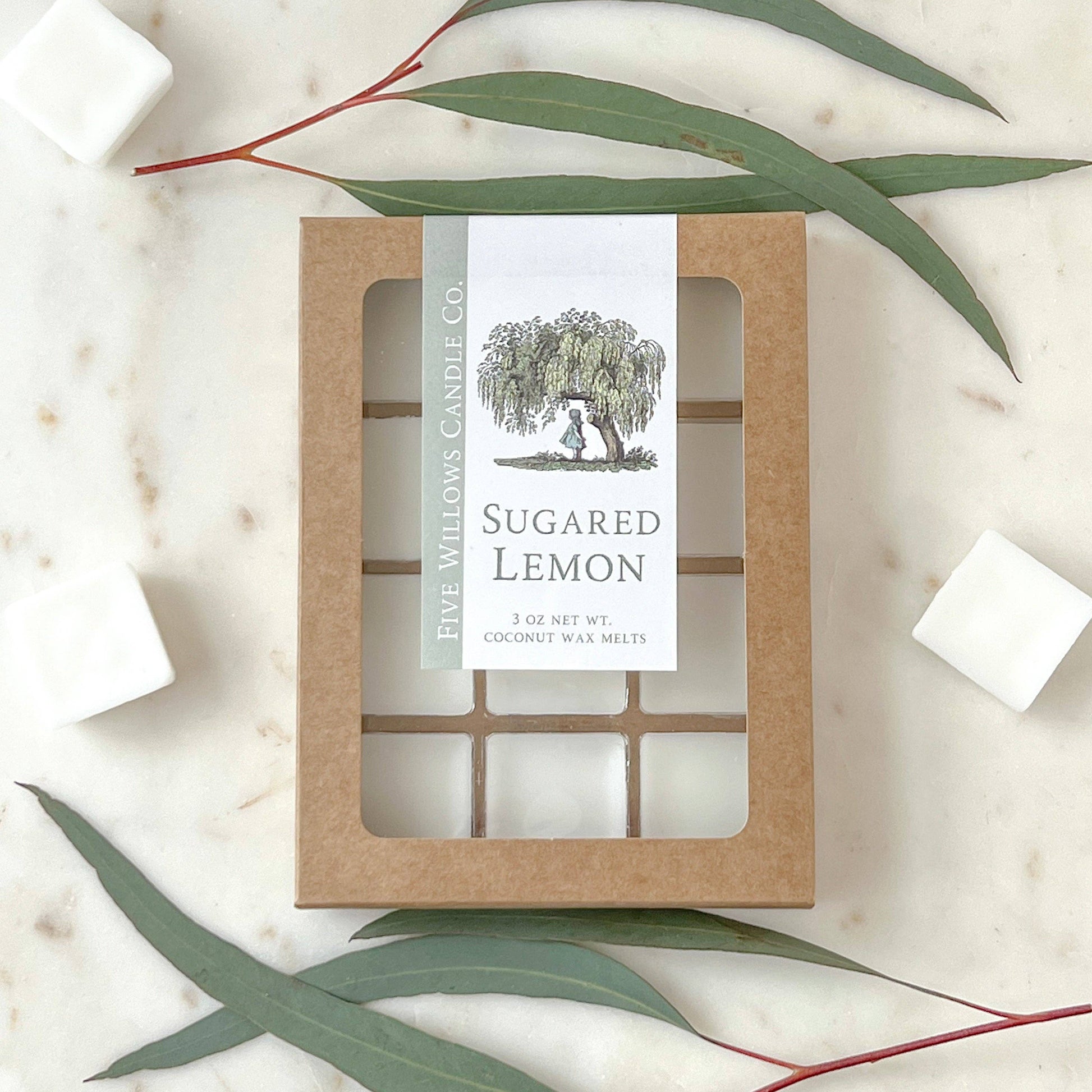 Sugared Lemon candle packaging with a label on a marble surface with eucalyptus leaves.